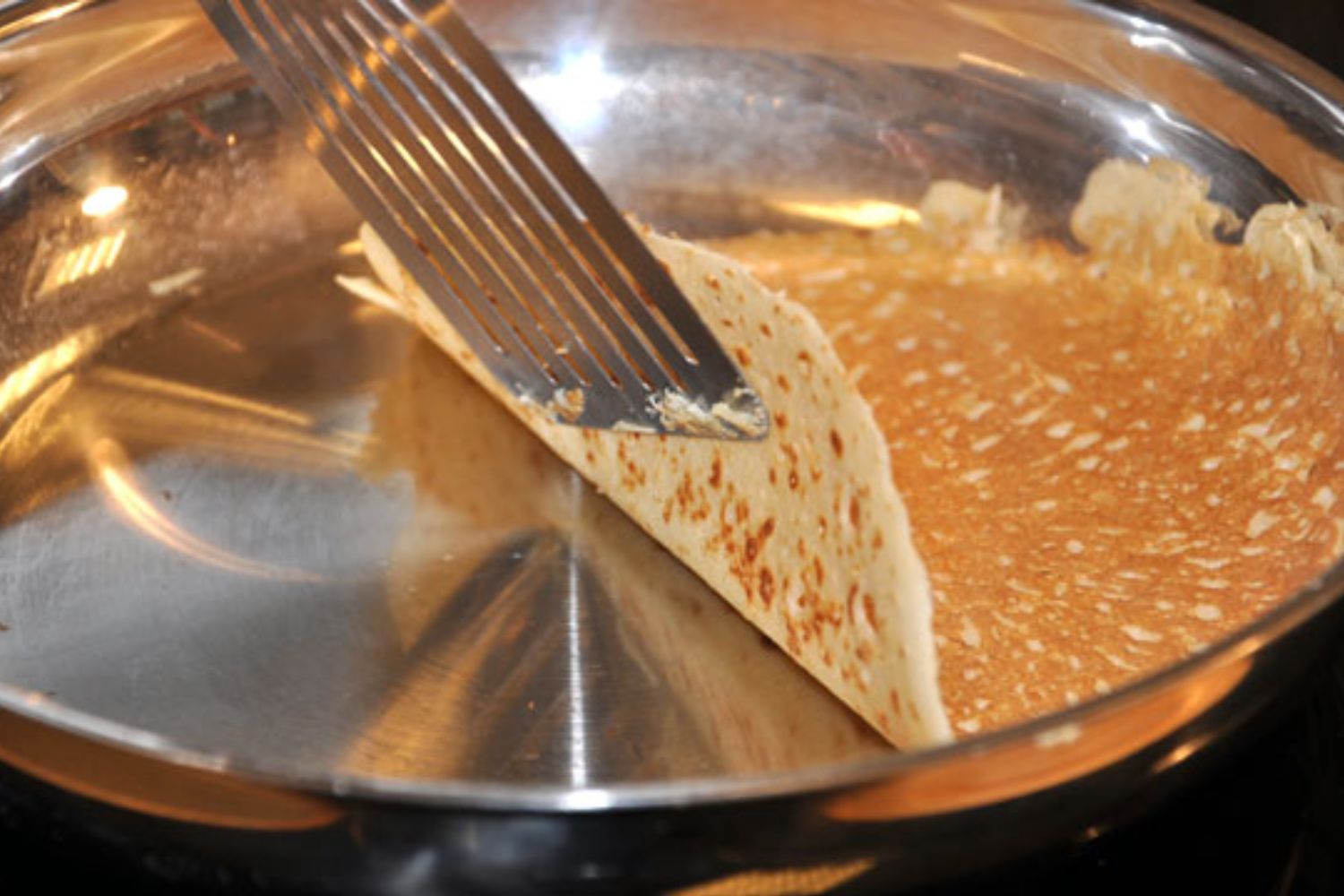 cuisinier qui fait une crêpe dans une poêle en inox