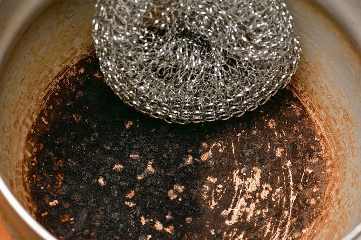 poêle en inox brulée avec un objet pour gratter celle-ci