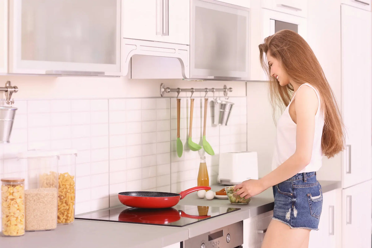 jeune femme dans une cuisine lumineuse entrain de faire a manger avec sa poele en ceramique rouge 