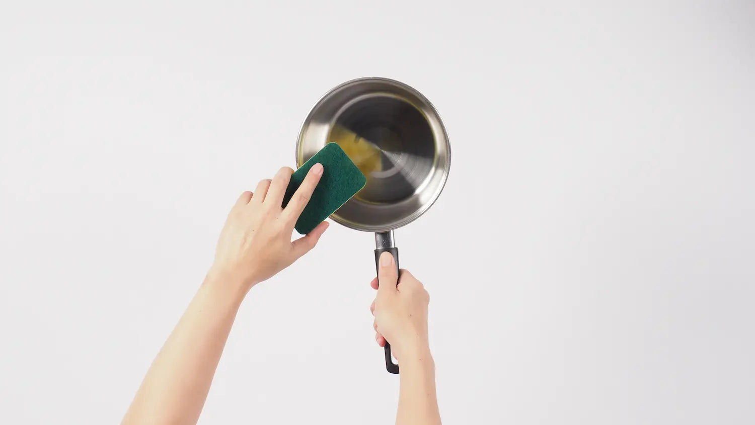 homme qui nettoie une poele en acier avec une eponge a tampon 