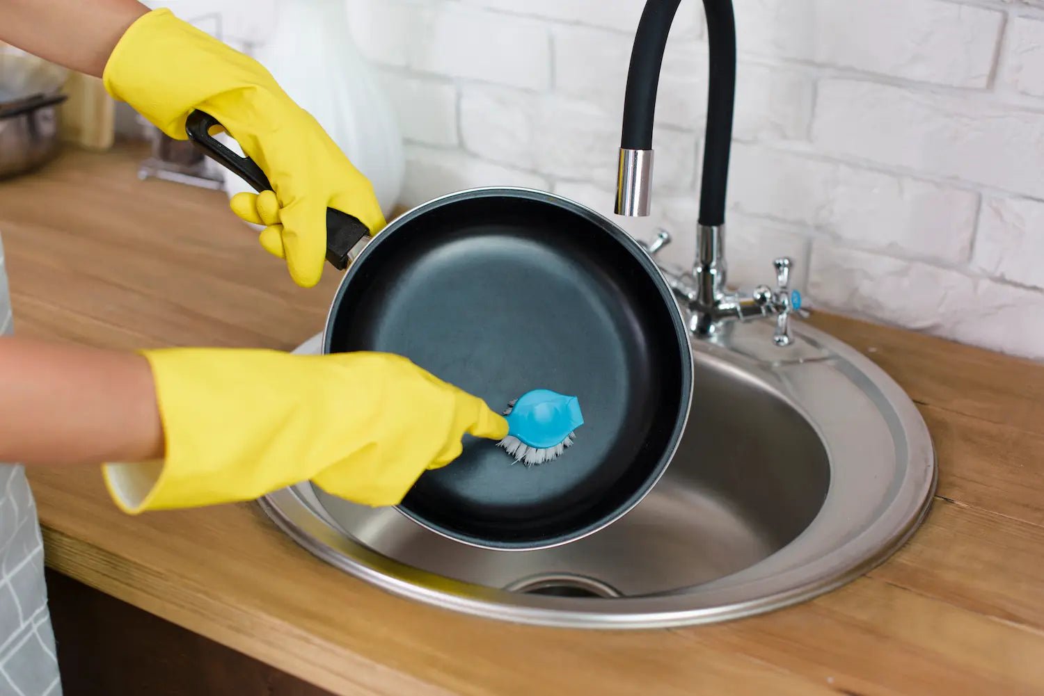 nettoyage d'une poele en teflon avec une brosse dans un évier en inox
