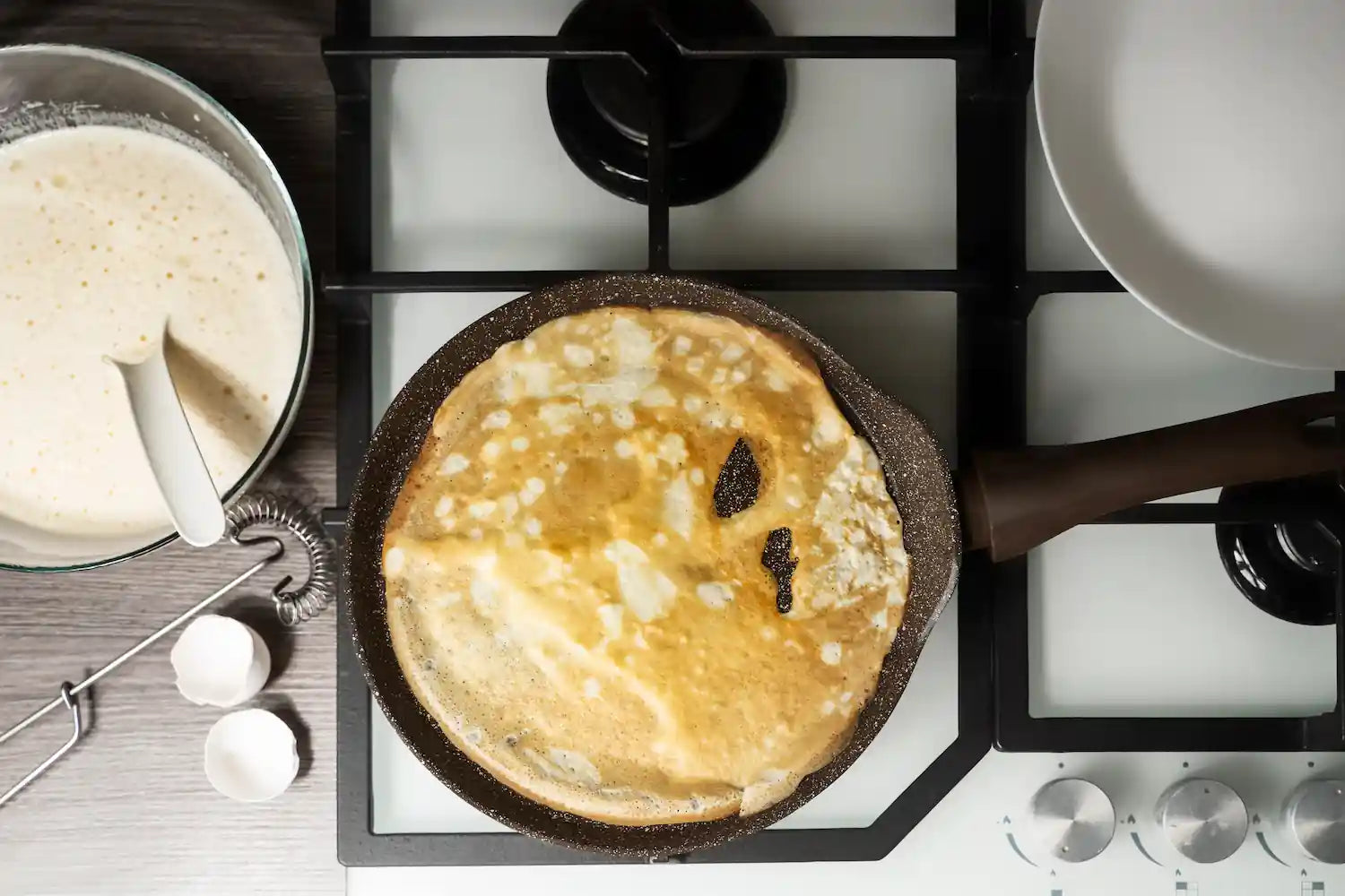 cuisson d'une crêpe dans une poêle sur une gazinière avec une pate a crêpe sur la gauche 