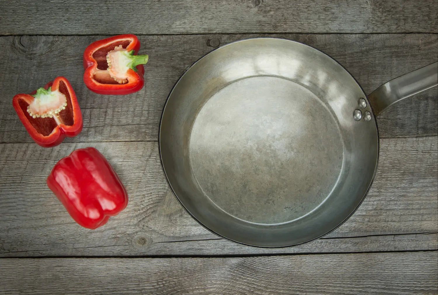 poele en acier sur une table en bois avec des poivrons rouge a coté 