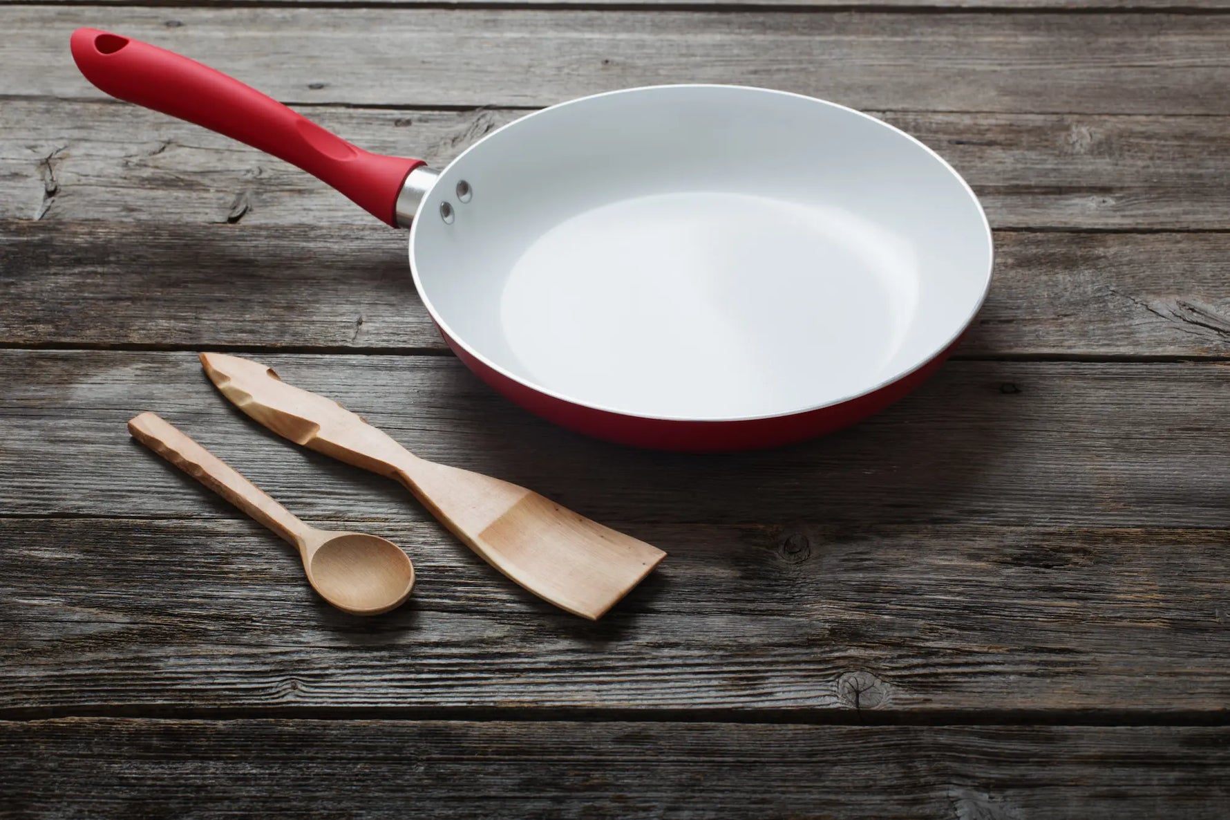 poele en ceramique blanc et rouge sur une table en bois foncé avec une cuillère et une spatule en bois