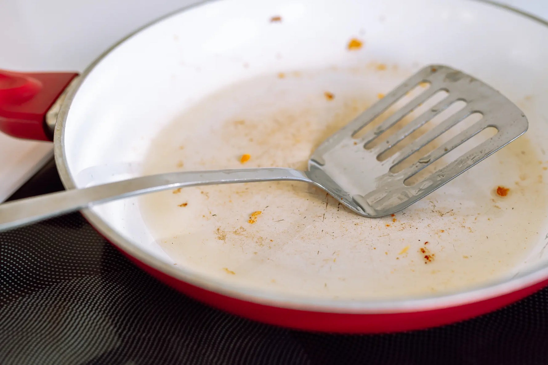 poele en ceramique blanche avec une spatule en inox sale