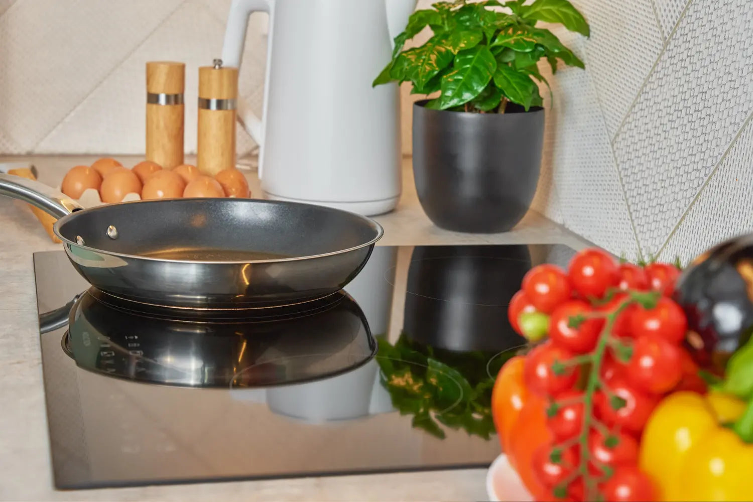 poele en inox sur une plaque à induction avec en avant plan des tomates et en arriere plan des oeufs du basilic et des epices