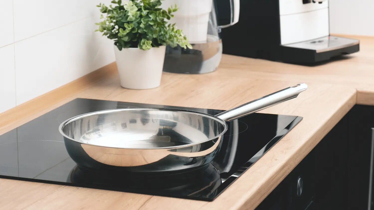 cuisine en bois avec une poele en inox sur une plaque vitrocéramique avec un pot de fleur en arrière plan
