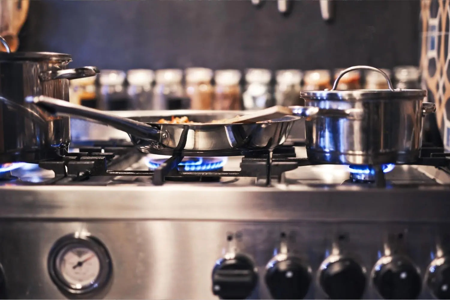 gaziniere dans une cuisine de chef avec une poele en inox et deux casseroles sur le feu 