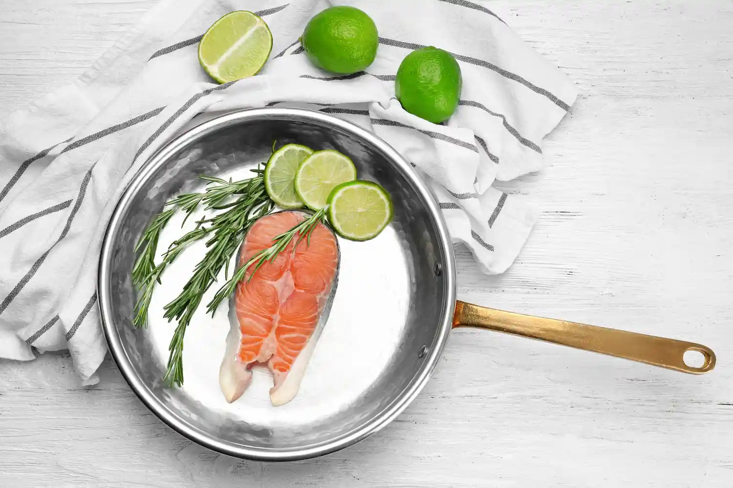 saumon et citron vert dans une poele en inox sur une table avec un torchon blanc