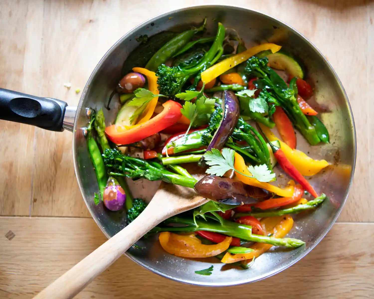 sauteuse en inox avec des légumes colorés entrain d'etre mélangé avec une spatule en bois