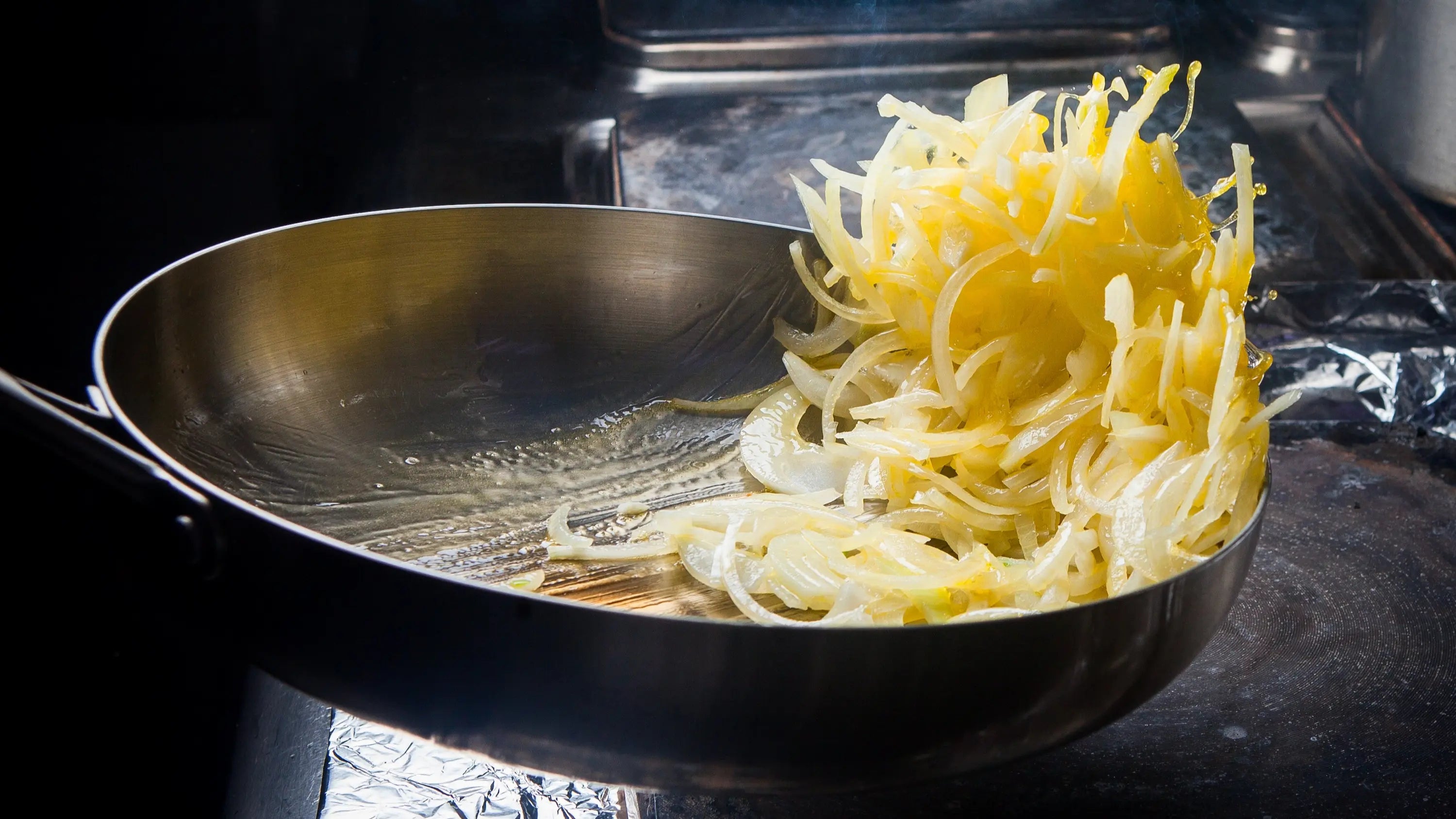 sauté d'oignon cuit dans une poêle en inox avec en arrière plan une cuisine de chef